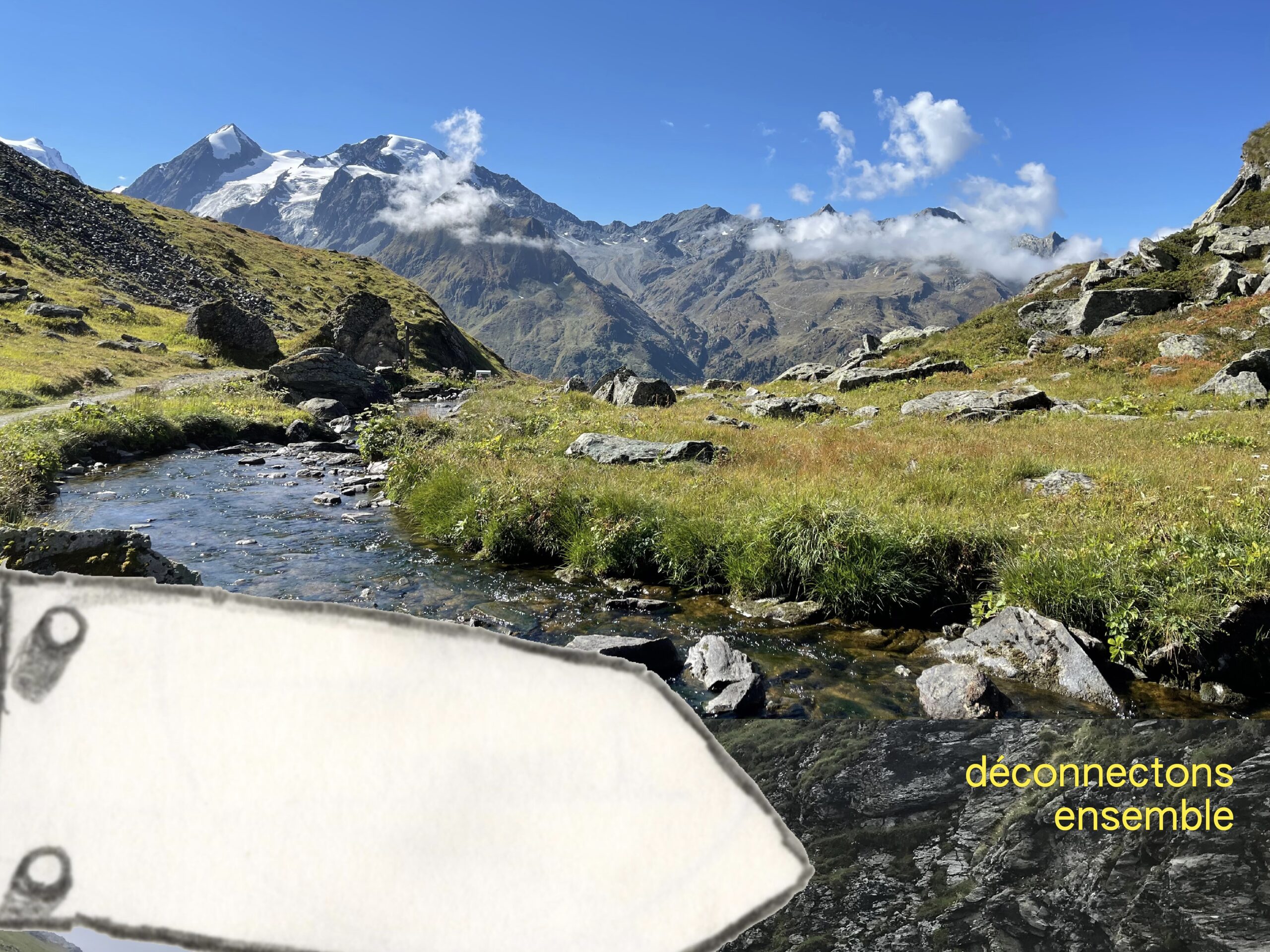 Paysage de montagne verdoyant avec un ruisseau et des sommets enneigés lors d'une rando créative à la Givrine pour se déconnecter de la technologie.
